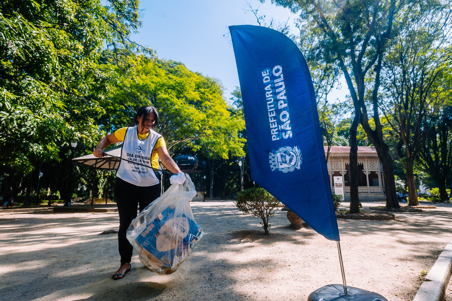 Voluntária no Mutirão Limpa Brasil ao lado de uma haste da Prefeitura de São Paulo.