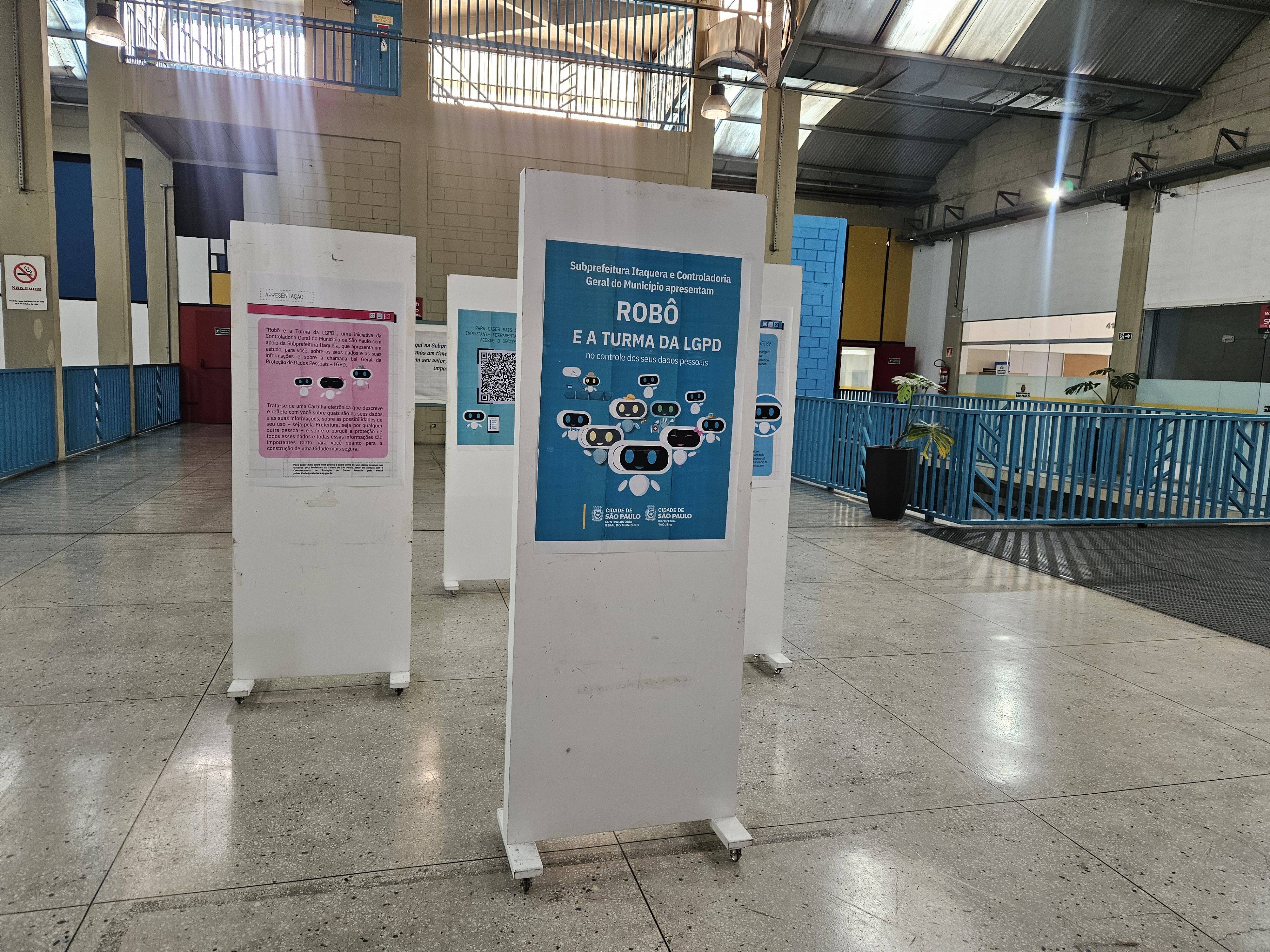 A imagem mostra um banner retangular na cor azul claro, com texto em branco e elementos gráficos. No topo, em letras grandes e com um design que sugere movimento. Abaixo, em letras menores e com um estilo diferente.  No canto superior direito, em um círculo branco com borda azul, há a palavra 