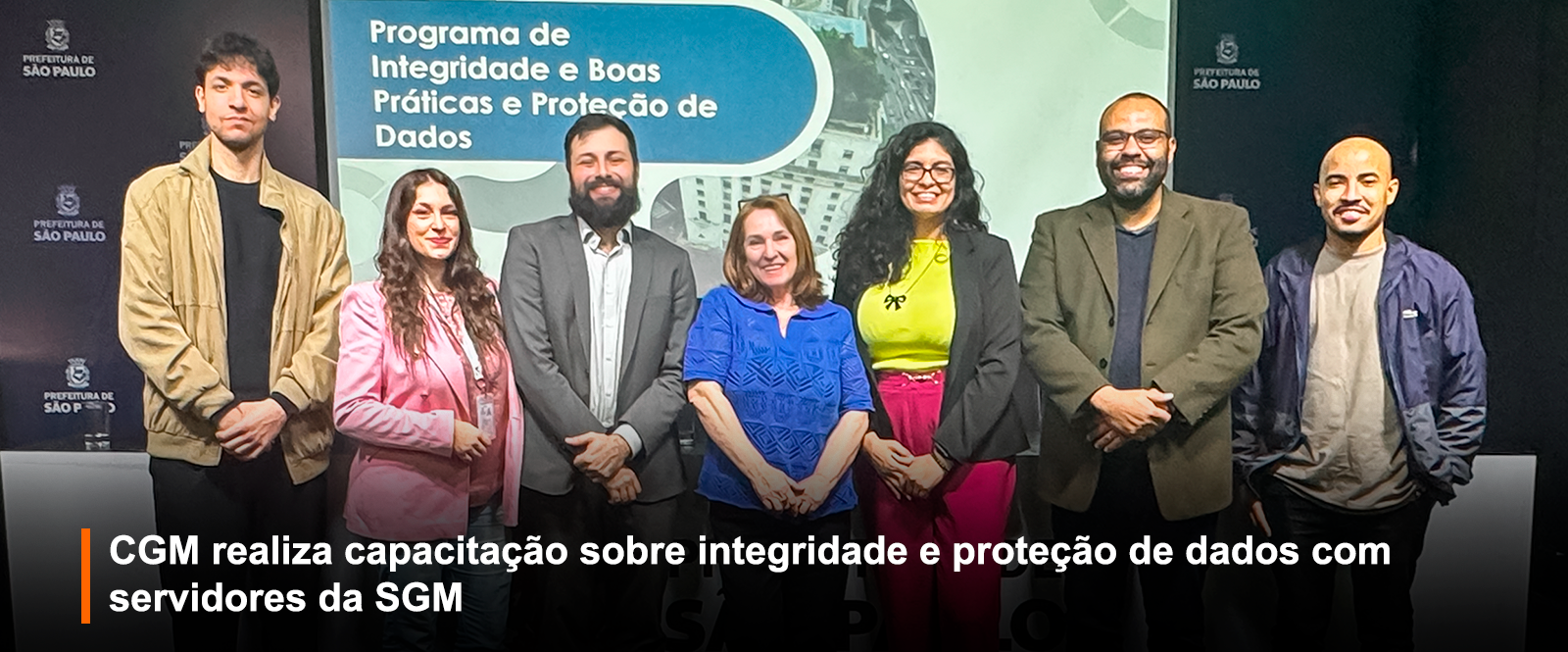 7 pessoas posando na foto após uma palestra, de fundo um telão branco.