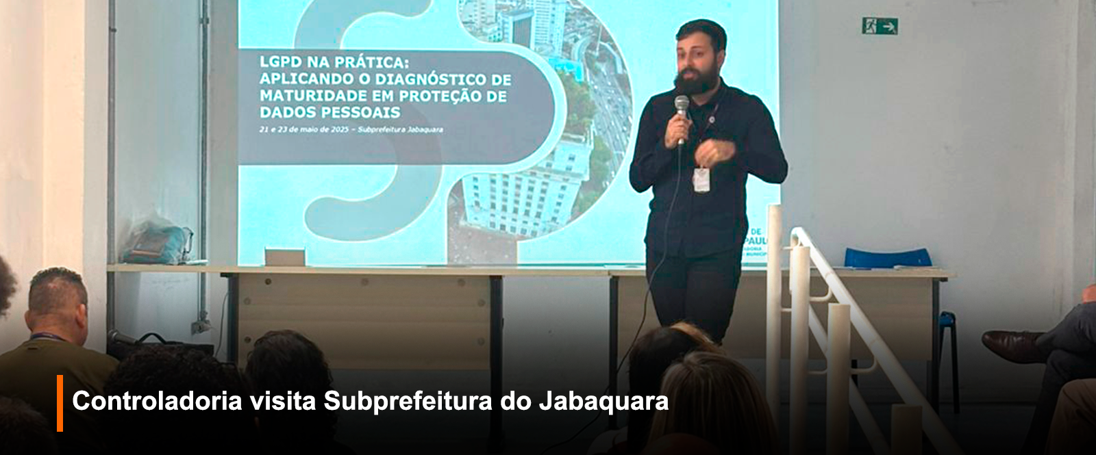 Fotografia de palestra em ambiente interno: homem com barba e camisa preta apresenta 