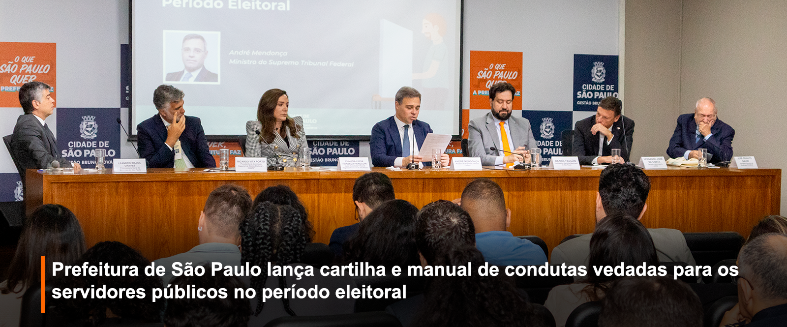 Fotografia de evento institucional em auditório: sete autoridades em mesa.