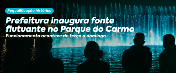 O post trata da inauguração da fonte flutuante no Parque do Carmo. A arte mostra uma fonte iluminada em tons de azul durante a noite, com diversos jatos d'água formando uma cortina ao fundo sobre o lago. Em primeiro plano, aparecem as silhuetas escuras de quatro pessoas observando o espetáculo de água e luz à beira do lago. A iluminação da fonte se reflete na superfície da água, destacando o contraste entre a claridade dos jatos e o ambiente noturno.